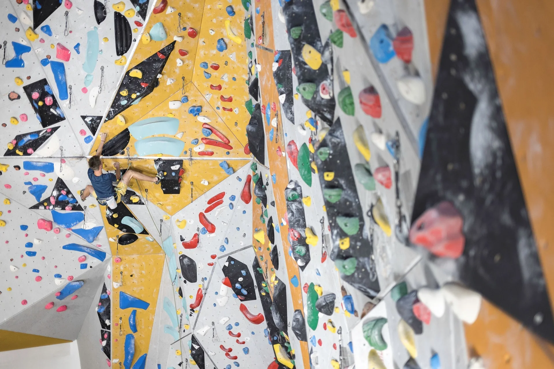 Bunte Griffe und Routen in einer Kletterhalle - in der Entfernung sieht man einen Sportler | © DAV / Jens Klatt